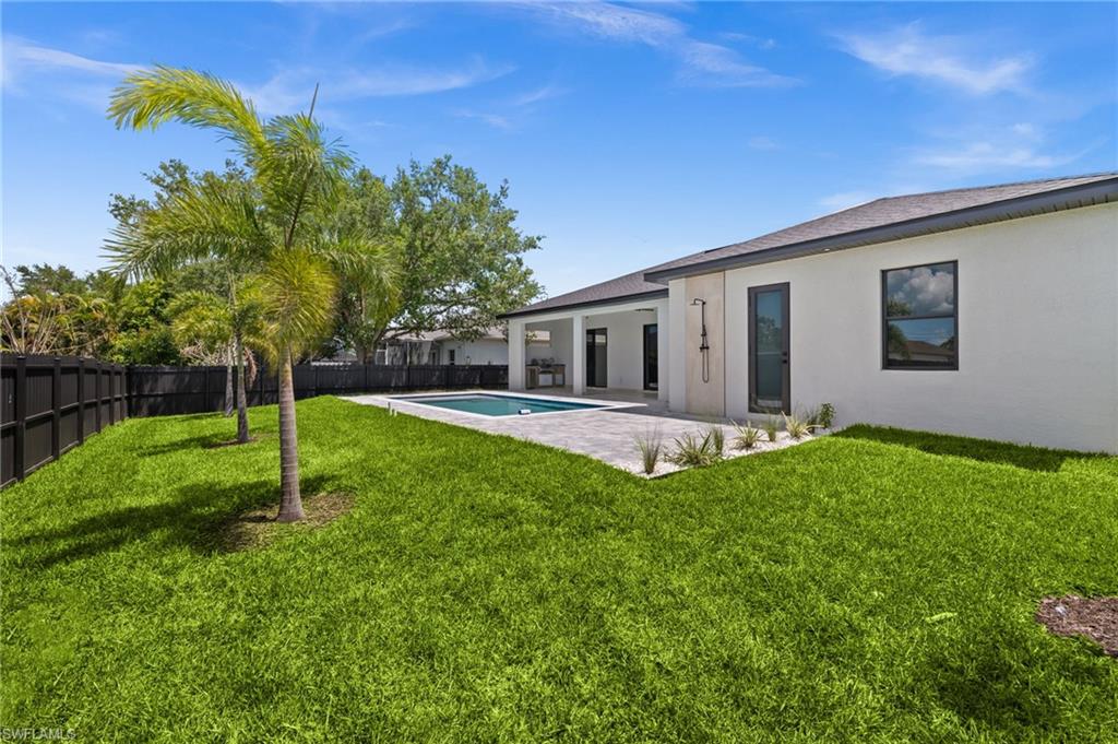 Expansive rear yard featuring a swimming pool, paved patio, vibrant lawn, and mature palm trees