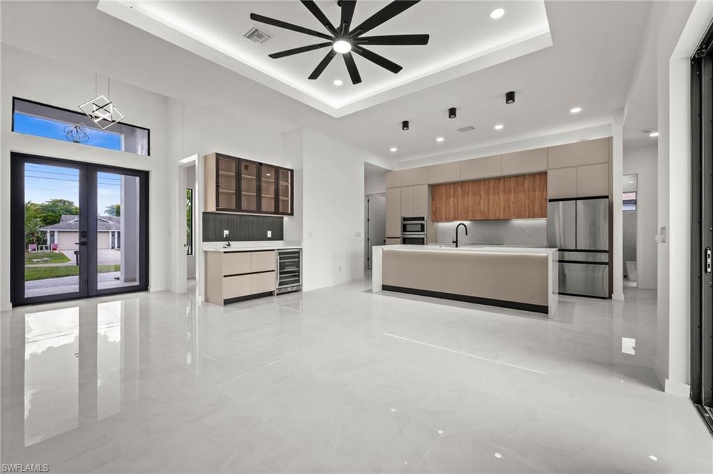 Open-concept living space with large format porcelain tile flooring and a tray ceiling featuring a ceiling fan and recessed lighting