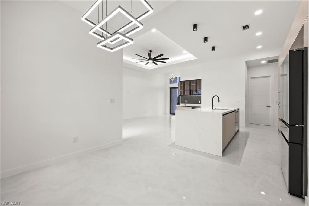 Open-concept living space featuring sleek tile flooring, a contemporary kitchen island with an integrated sink and matte black faucet, and modern square pendant lighting