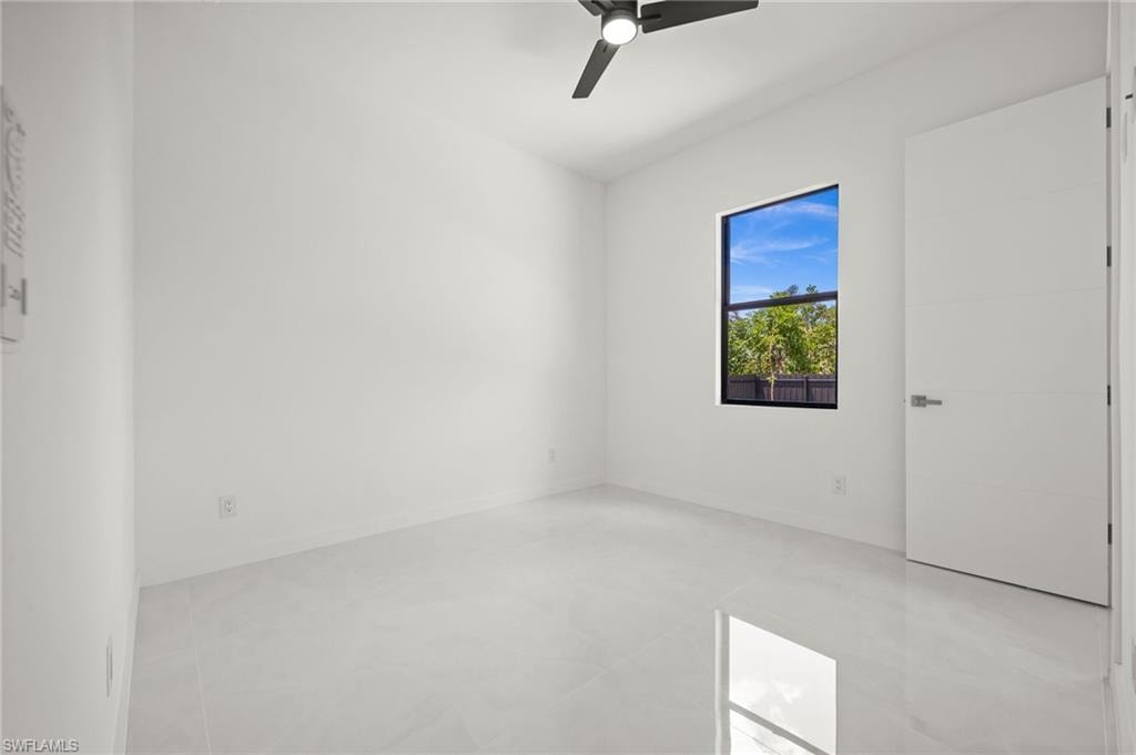 Spacious room featuring white walls, large format tile flooring, a black ceiling fan, a prominent window with black trim, and a white flat panel door with chrome hardware
