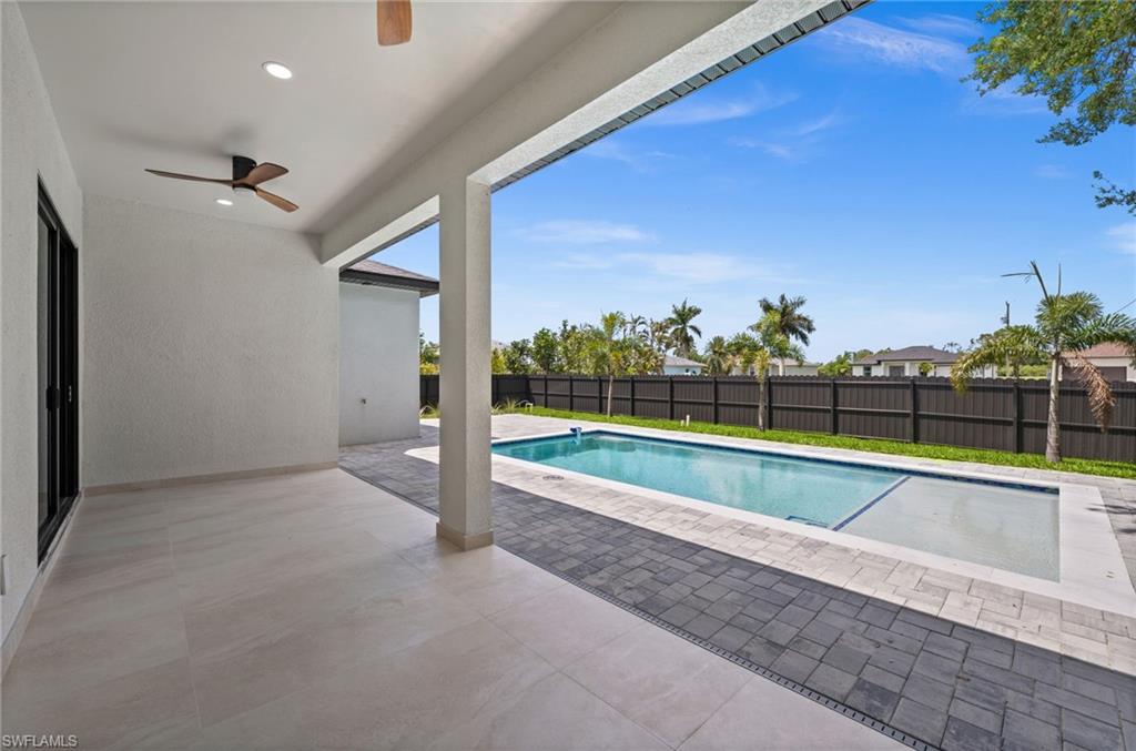Expansive outdoor living area featuring a covered patio with recessed lighting and a ceiling fan, opening to a rectangular swimming pool with a sun shelf