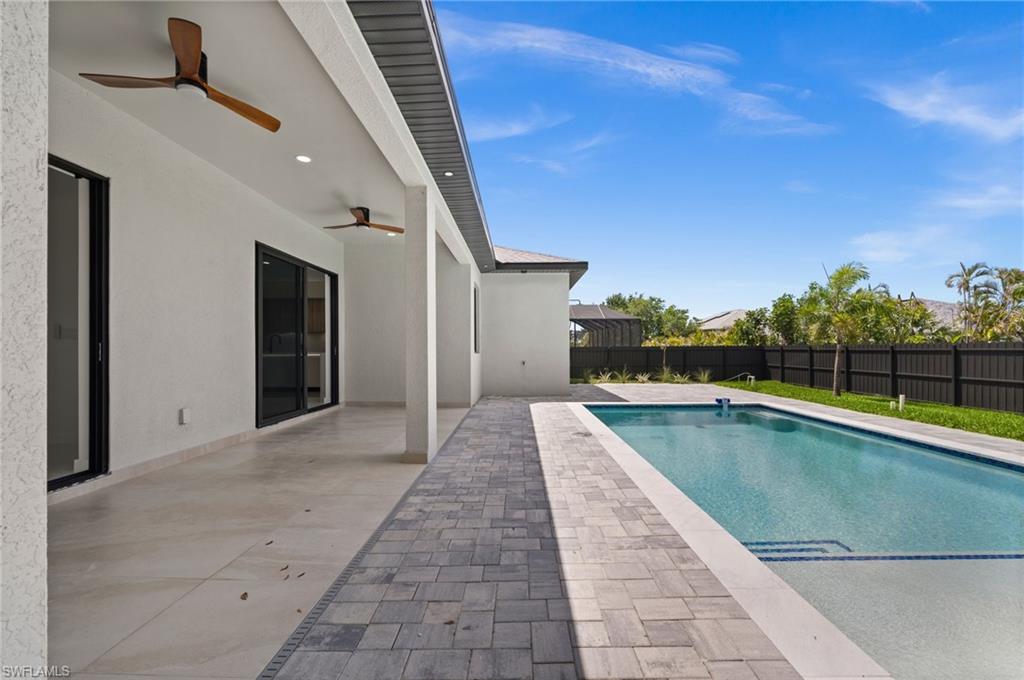 Rear exterior featuring a covered patio with recessed lighting and ceiling fans, leading to a paver patio and a rectangular swimming pool