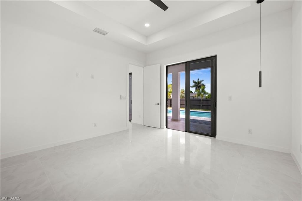 Spacious interior room featuring white walls, large format light-toned tile flooring, and a tray ceiling