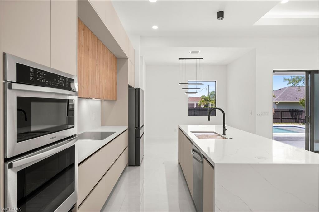 Contemporary kitchen featuring integrated stainless steel appliances, a built-in oven and microwave combination, and a large center island with an undermount sink and matte black faucet
