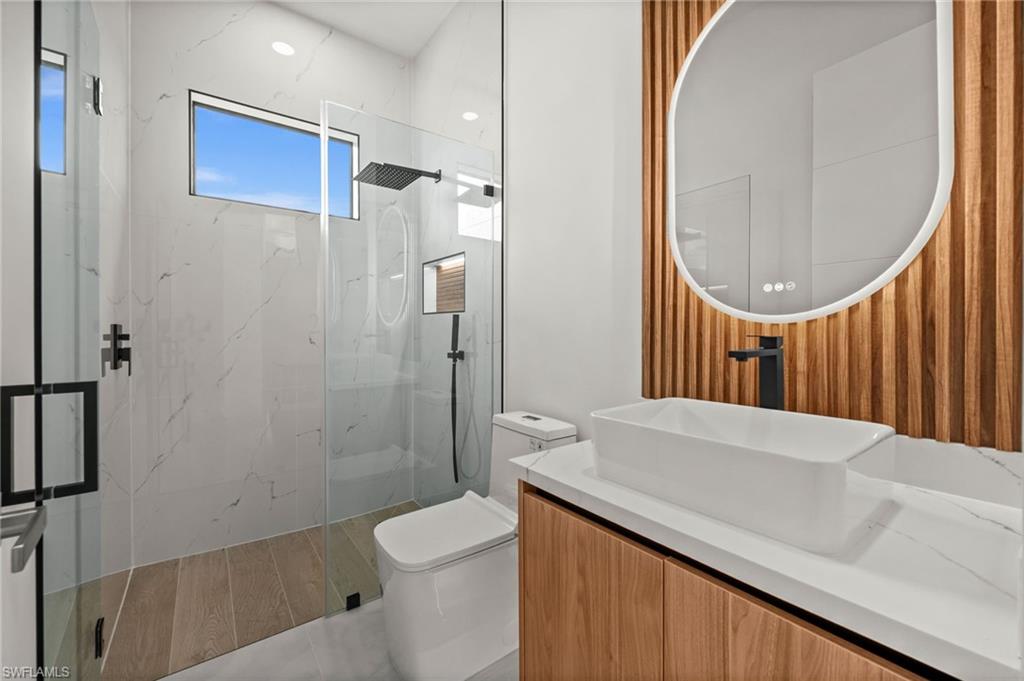 Contemporary bathroom featuring a floating wood-finish vanity with a rectangular vessel sink, an oval backlit mirror, and a glass-enclosed shower with a rainfall showerhead