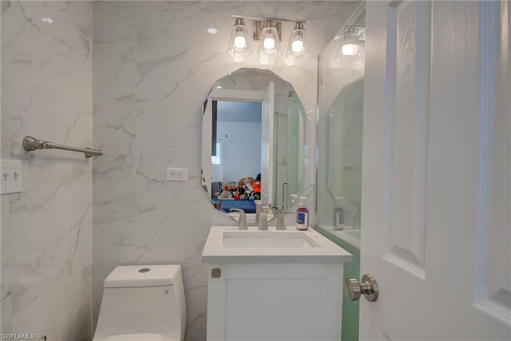 Bathroom featuring full-height marble-look tile, contemporary vanity with integrated sink, brushed nickel faucet, and a decorative frameless mirror