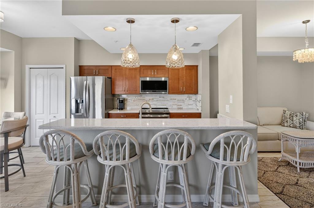 Kitchen featuring a breakfast bar with stone countertop, stainless steel appliances, wood cabinetry, and a tile backsplash