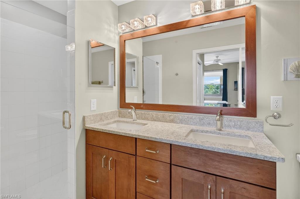 Dual vanity with integrated sinks, granite countertop, wood-finish cabinetry, and framed mirror