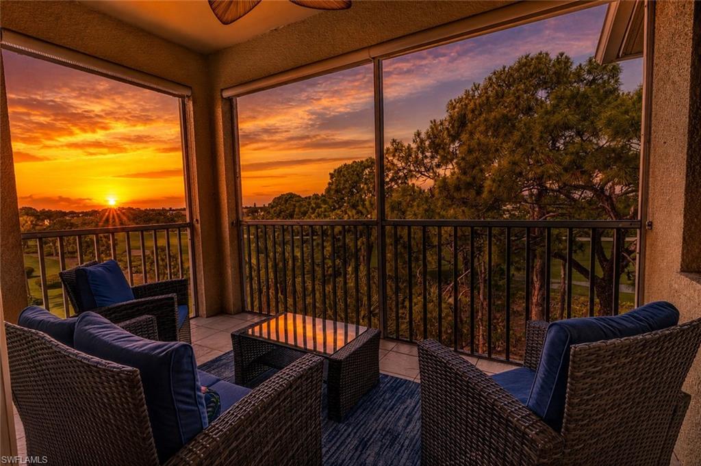 Screened balcony featuring a tiled floor, dark railing, and a scenic sunset backdrop over distant trees and a golf course