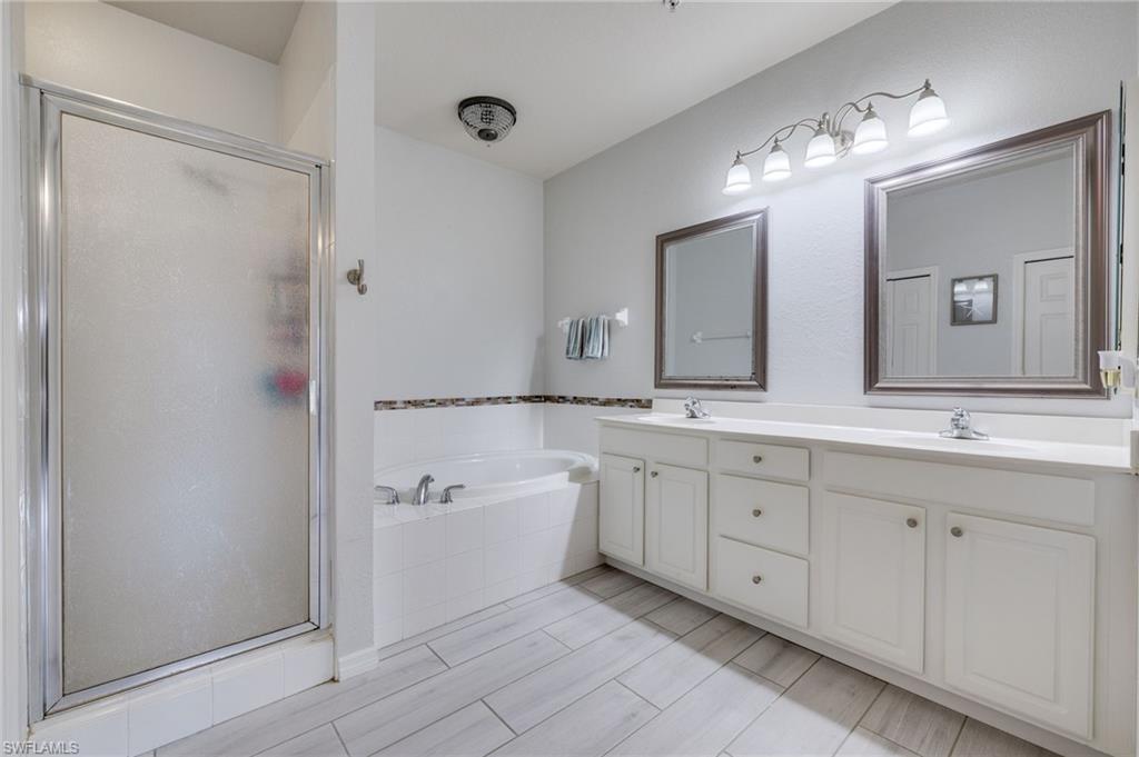 Spacious bathroom featuring a dual vanity with white cabinetry, a built-in soaking tub, a separate shower with a frosted glass enclosure, and light wood-finish plank flooring