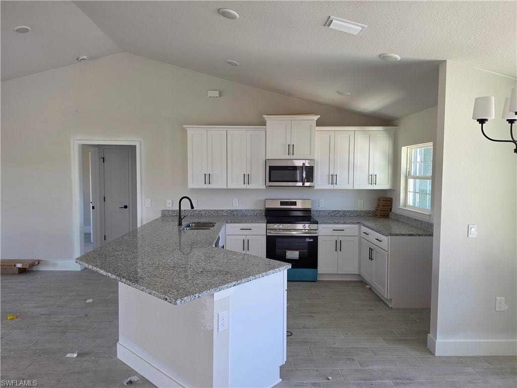 Kitchen featuring white shaker cabinetry, stainless steel appliances, granite countertops, and a central island with an undermount sink