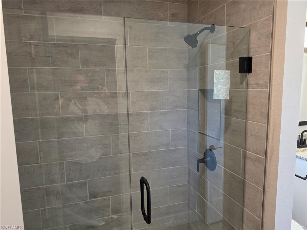 Glass-enclosed shower featuring large format tile surround, matte black shower fixtures, and a coordinating matte black handle