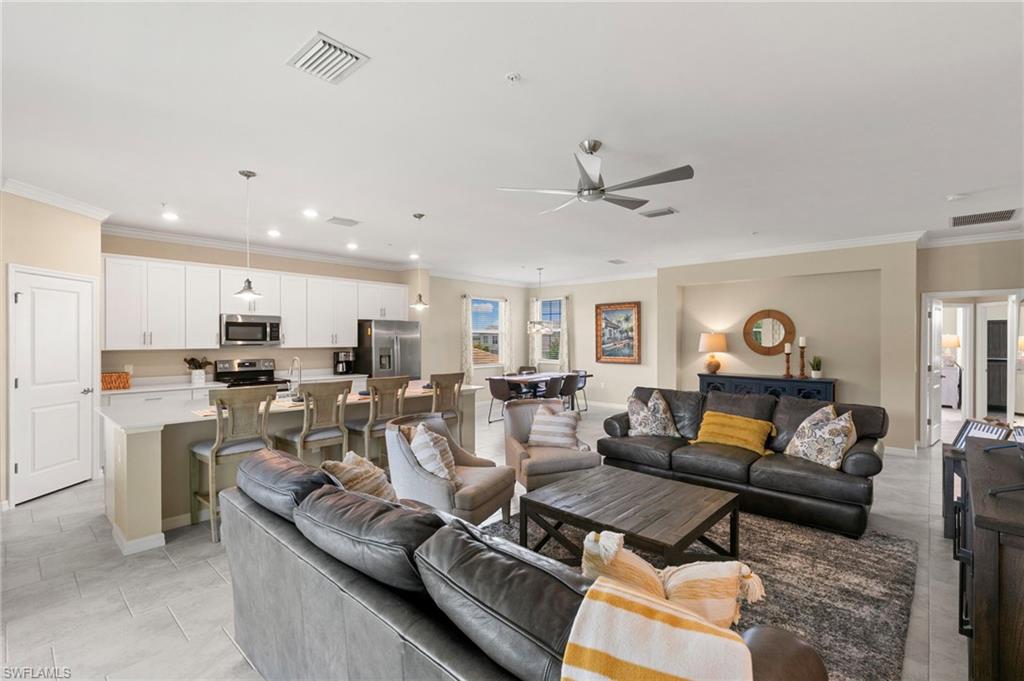 Open-concept living space featuring light tile flooring, a contemporary ceiling fan, recessed lighting, a kitchen island with pendant lighting, and white cabinetry with stainless steel appliances