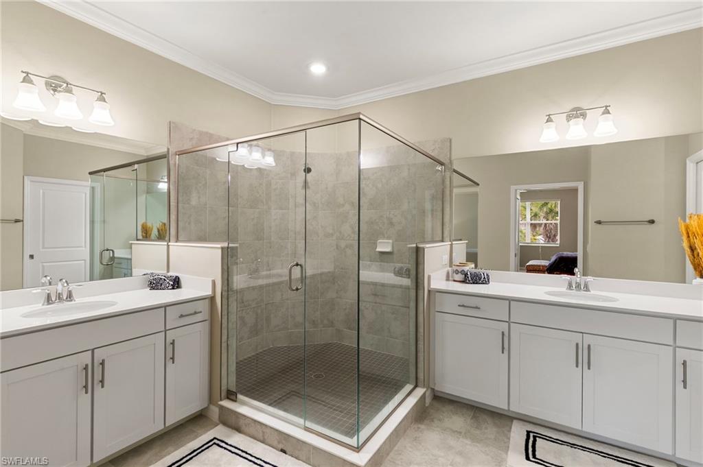 Spacious bathroom featuring a glass-enclosed shower with tile surround, dual vanities with white cabinetry and integrated sinks, extensive mirror coverage, and crown molding