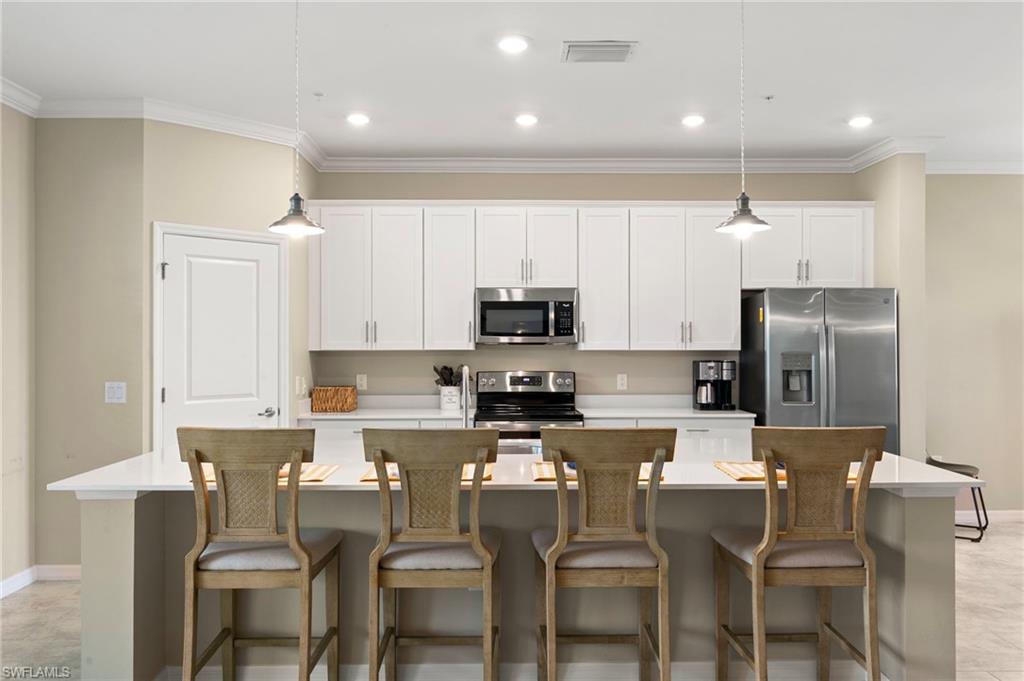 Bright kitchen featuring white shaker cabinetry, stainless steel appliances, a white countertop island with seating, recessed lighting, and pendant lighting fixtures