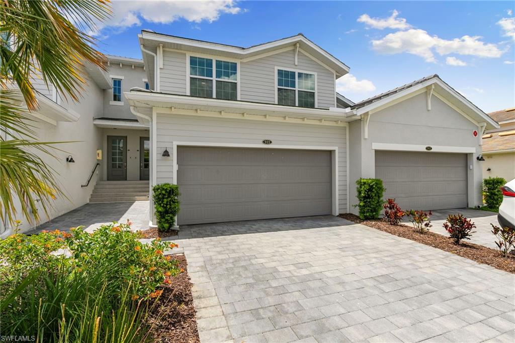 Contemporary two-story exterior featuring a light gray and white facade, dual garage doors, and a paver driveway