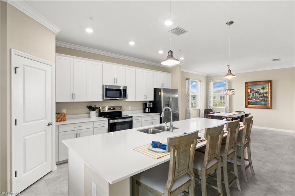 Kitchen featuring an expansive center island with an integrated sink, stainless steel appliances, white cabinetry, and light-toned flooring