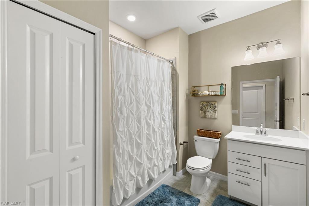 Bathroom featuring a single vanity with white cabinetry, a built-in toilet, a shower with a shower curtain, a large mirror, and recessed lighting