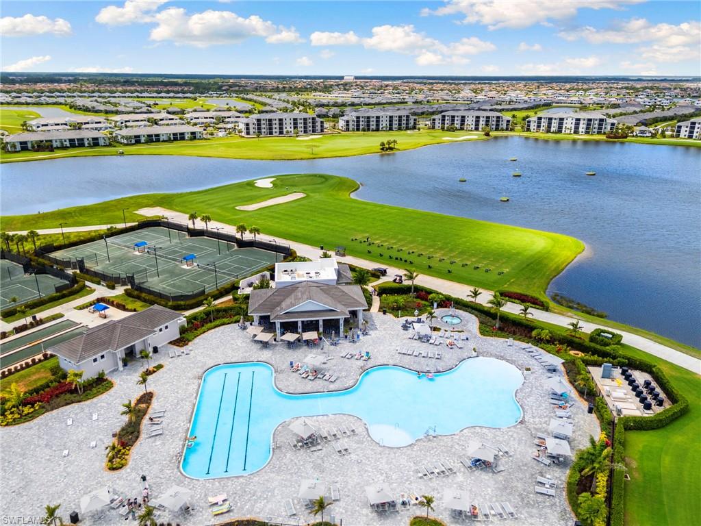 Expansive aerial showcasing a large resort-style pool area, multiple tennis courts, and a golf course bordering a significant body of water