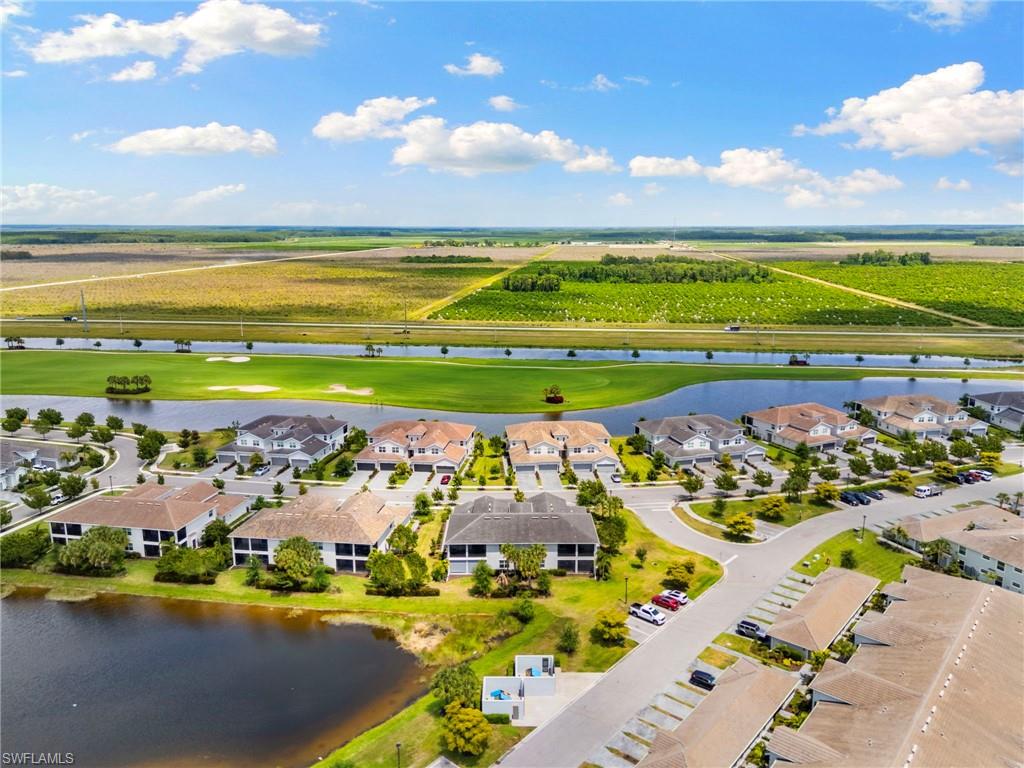 Aerial perspective of a residential community featuring multiple two-story buildings with screened patios, surrounded by mature landscaping and a large pond