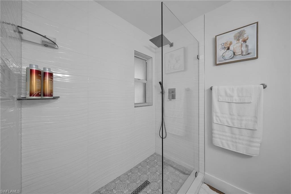 Glass-enclosed shower featuring white textured tile walls, a patterned tile floor, and a rain shower head