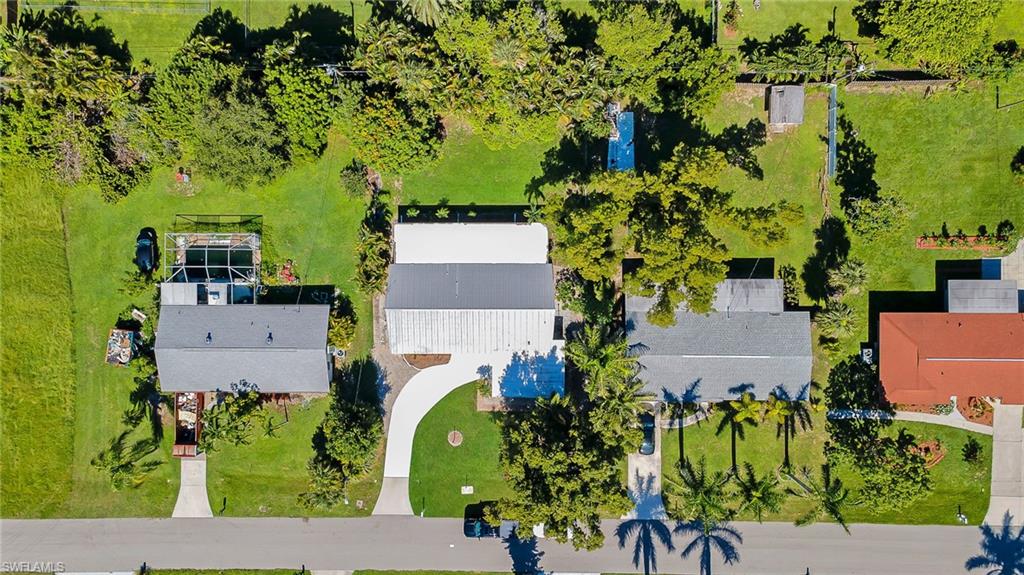 Aerial overview showcasing a property with a screen-enclosed pool, expansive green spaces, mature trees, and a paved driveway