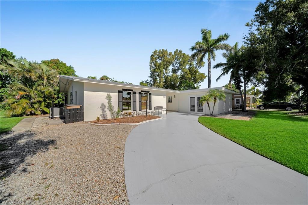 White stucco exterior with black window shutters and a curved paved driveway