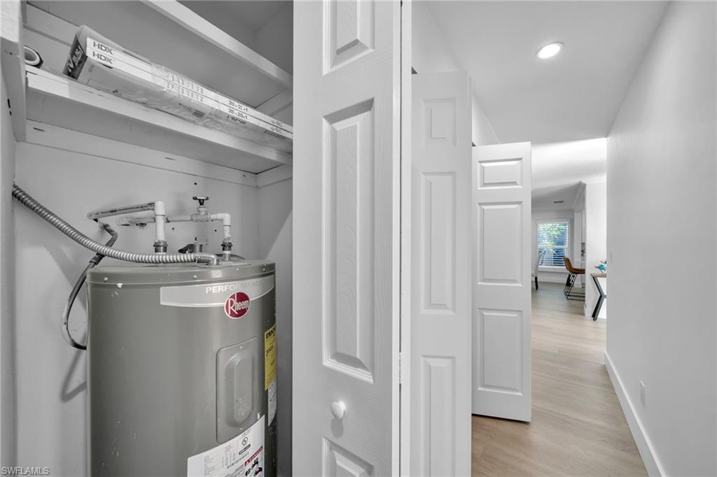 Utility closet featuring a water heater and shelving, with a hallway showcasing light wood-finish flooring and white paneled doors