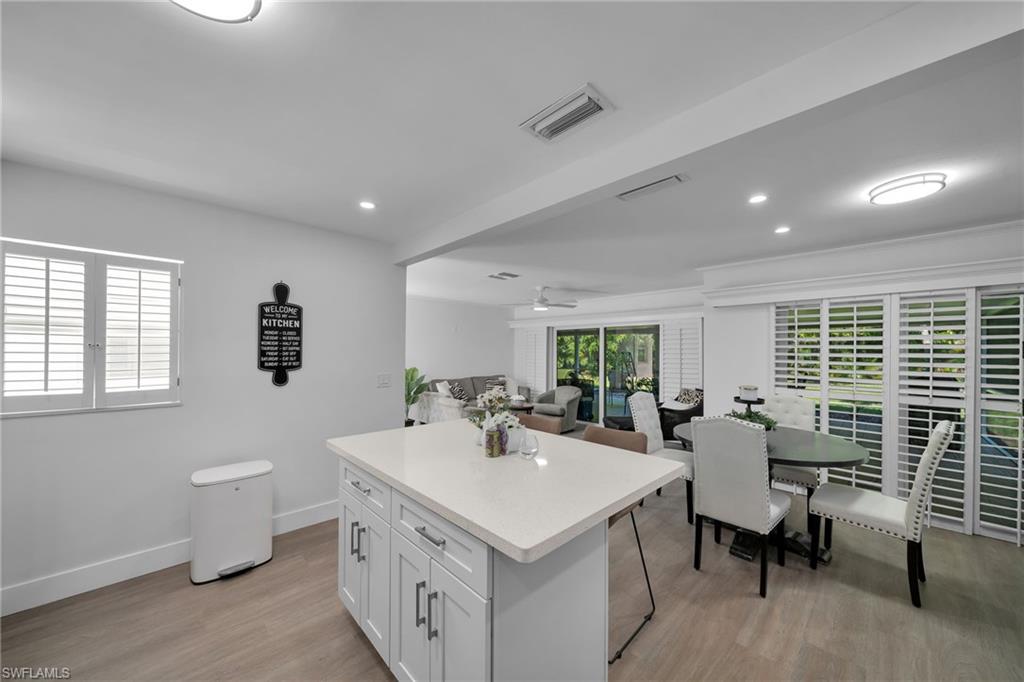 Kitchen featuring a large island with a light-toned countertop, wood-finish flooring, recessed lighting, and a window with plantation shutters