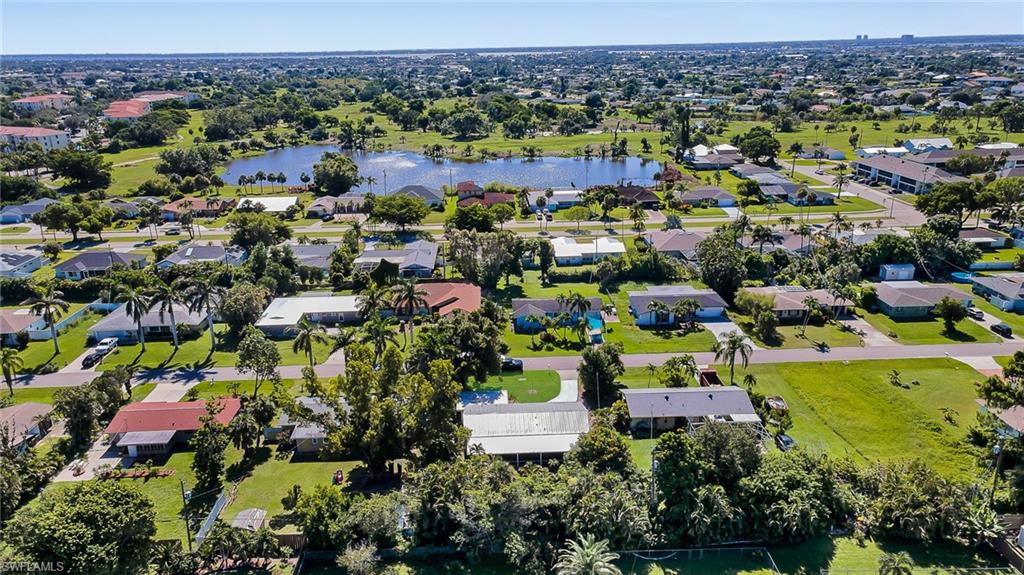 Aerial perspective showcasing a residential area with varied home styles, expansive green lawns, mature trees, and a prominent lake with a fountain