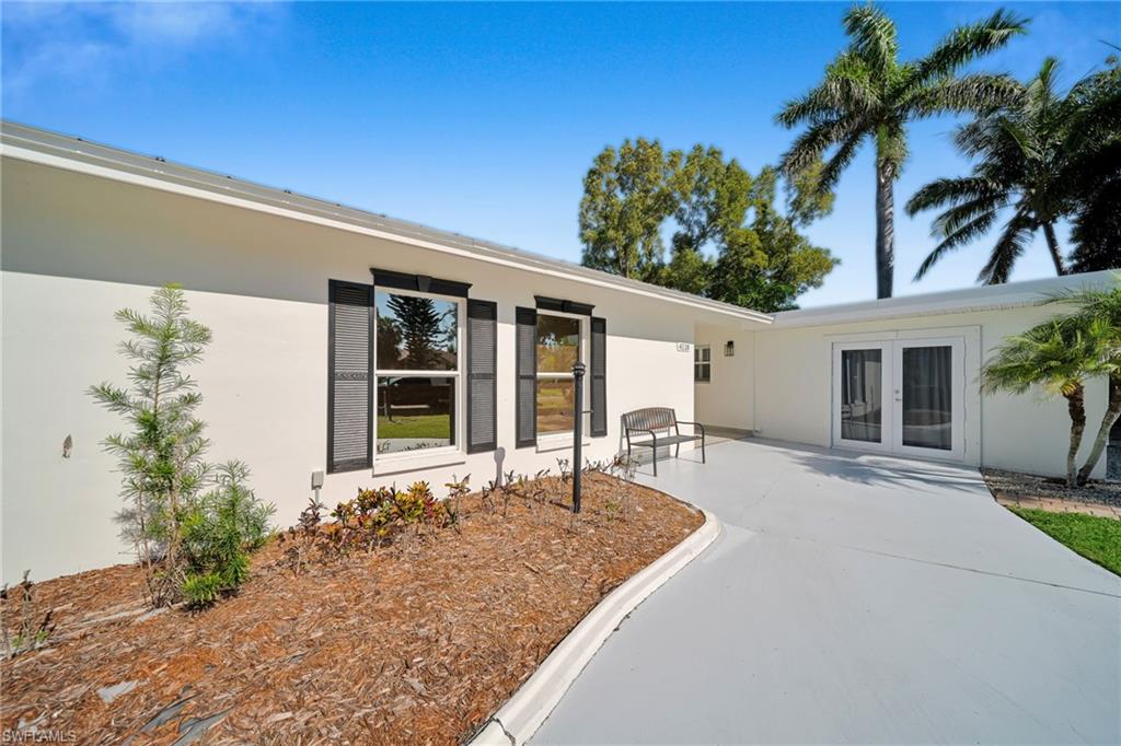 Light-colored stucco exterior featuring dark shutters, a low-sloped roofline, and mature landscaping