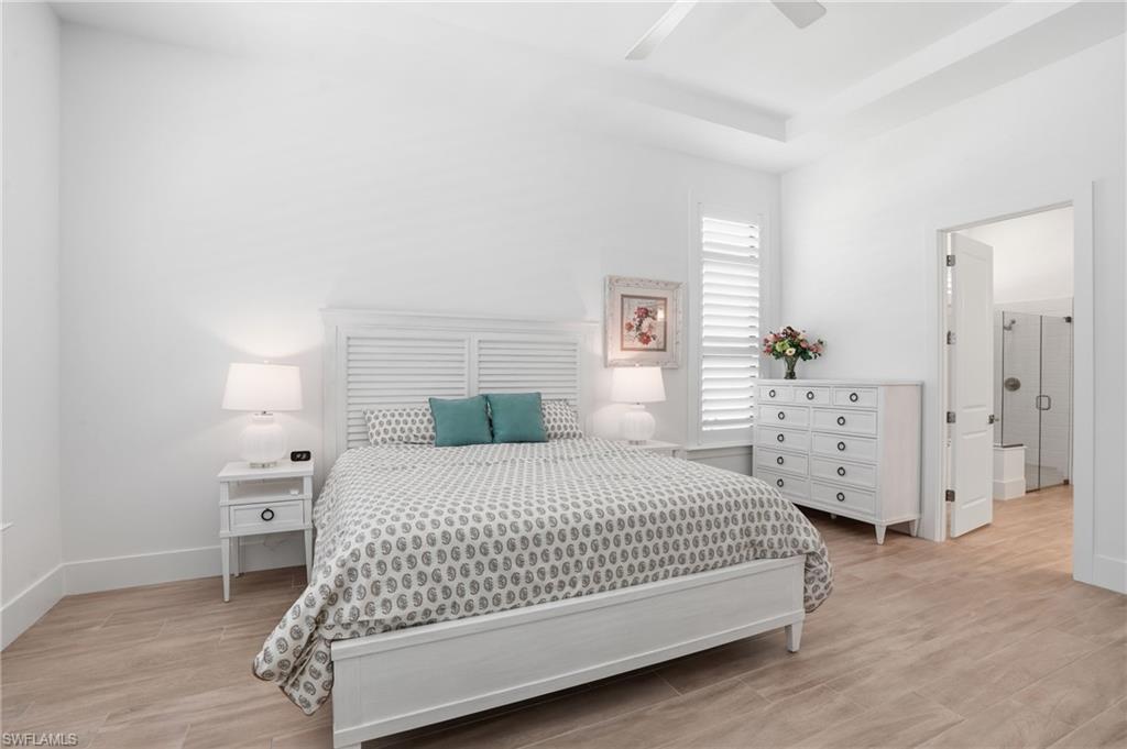 Bedroom featuring coffered ceiling, wood-look flooring, plantation shutters, and an en-suite bathroom with a glass-enclosed shower