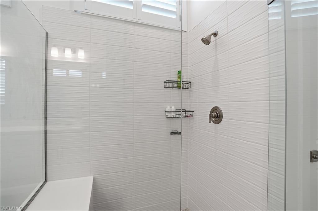 Shower with textured white tile walls, brushed nickel fixtures, glass enclosure, and an integrated bench