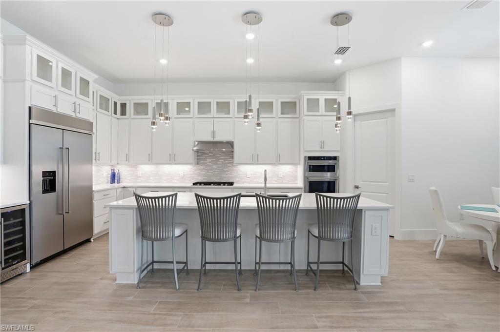 Gourmet kitchen featuring a central island with seating, stainless steel appliances, extensive white cabinetry with upper glass-front accents, a mosaic tile backsplash, and recessed and pendant lighting
