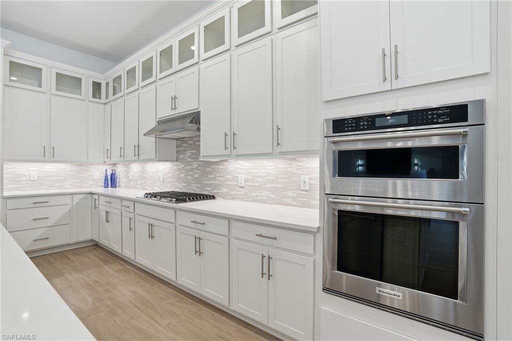 Sleek kitchen featuring white shaker cabinetry, stainless steel appliances, a gas cooktop, quartz countertops, and wood-finish flooring
