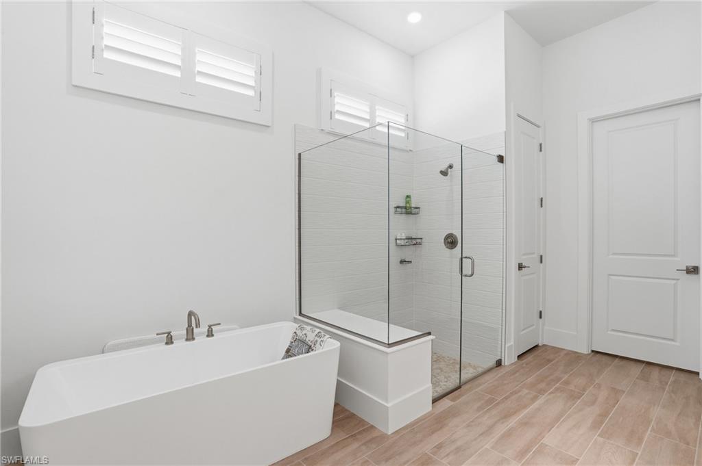 Spacious bathroom featuring a frameless glass shower enclosure, a contemporary freestanding tub with brushed nickel fixtures, and wood-finish tile flooring