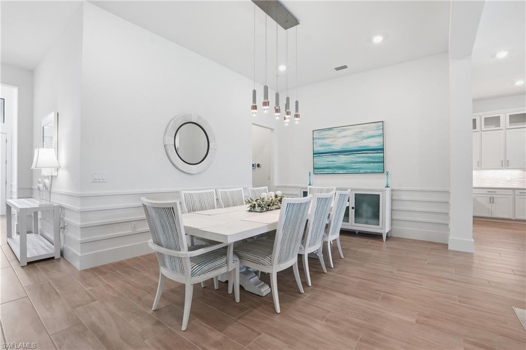 Dining area featuring wood-finish flooring, white wainscoting, and a linear pendant light fixture