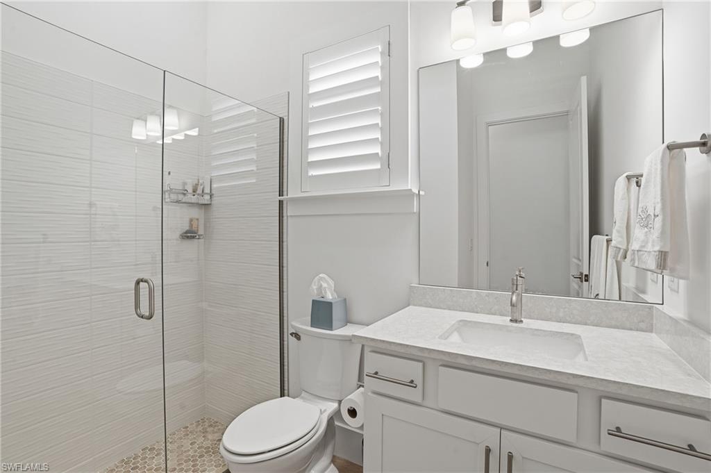 Contemporary bathroom featuring a glass-enclosed shower with textured tile, a single vanity with a solid surface countertop, an undermount sink, and a brushed nickel faucet