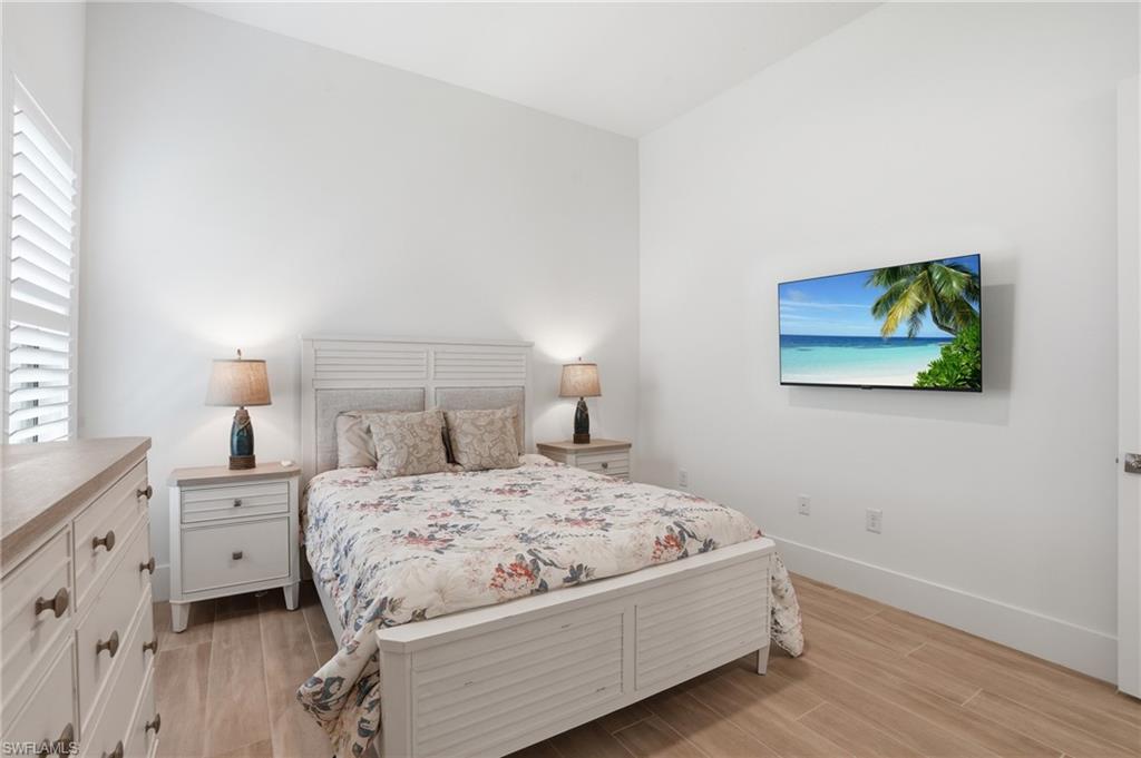Bedroom featuring wood-finish flooring, plantation shutters, and a wall-mounted television