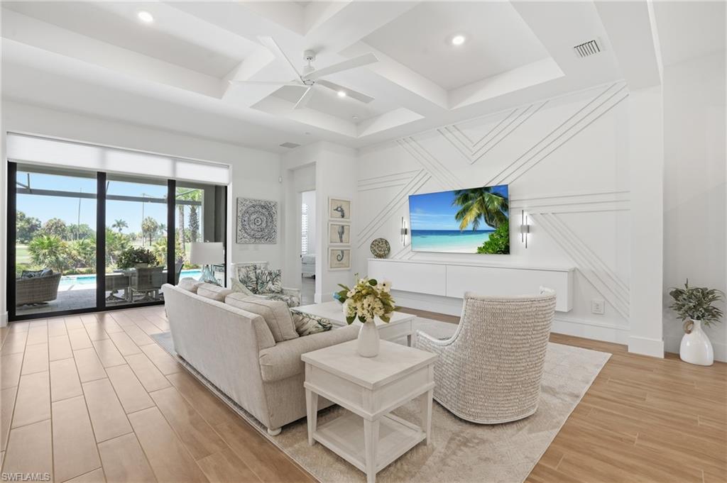 Expansive living area featuring coffered ceilings, wood-finish flooring, and a decorative accent wall