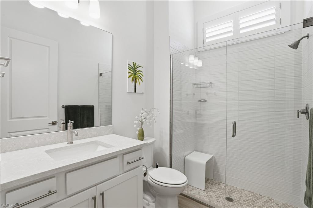 Bathroom featuring a single vanity with stone-finish countertop and undermount sink, a large frameless mirror, and a glass-enclosed shower