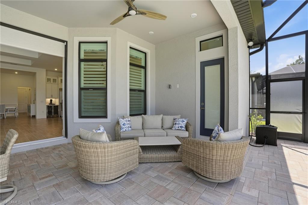 Screened outdoor living area featuring a ceiling fan, bay window with louvered panels, a full-lite exterior door, and large format paver flooring