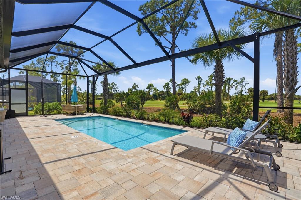 Screened lanai featuring a rectangular swimming pool, paver deck, and extensive landscaping
