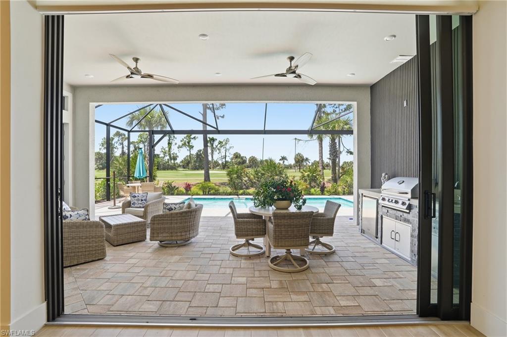 Expansive covered patio featuring patterned paver flooring, a built-in outdoor kitchen with grill, and ceiling fans