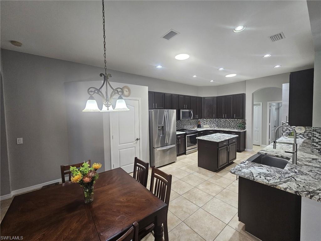 Kitchen featuring dark wood cabinetry, stainless steel appliances, a center island, granite countertops, and a patterned tile backsplash