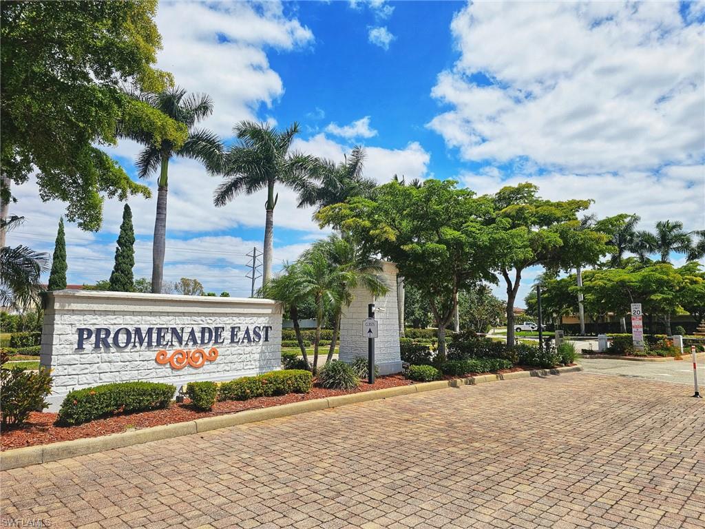 Community entrance featuring a stone-clad monument sign, mature tropical landscaping, and a paver drive