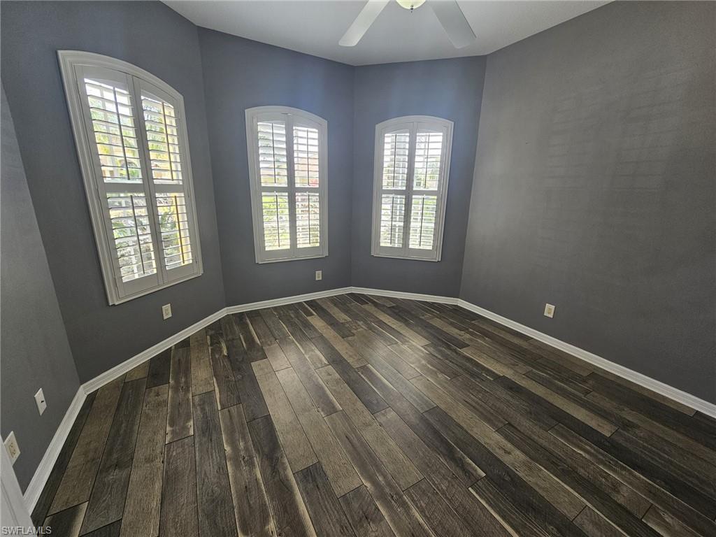 Room featuring three arched windows with plantation shutters, wood-finish flooring, and a ceiling fan