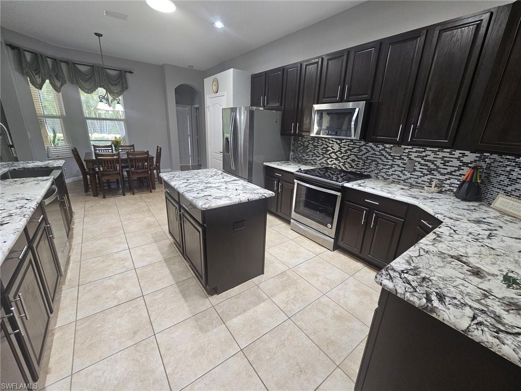 Spacious kitchen featuring dark wood cabinetry, light-toned tiled flooring, and a central island with a light-colored countertop