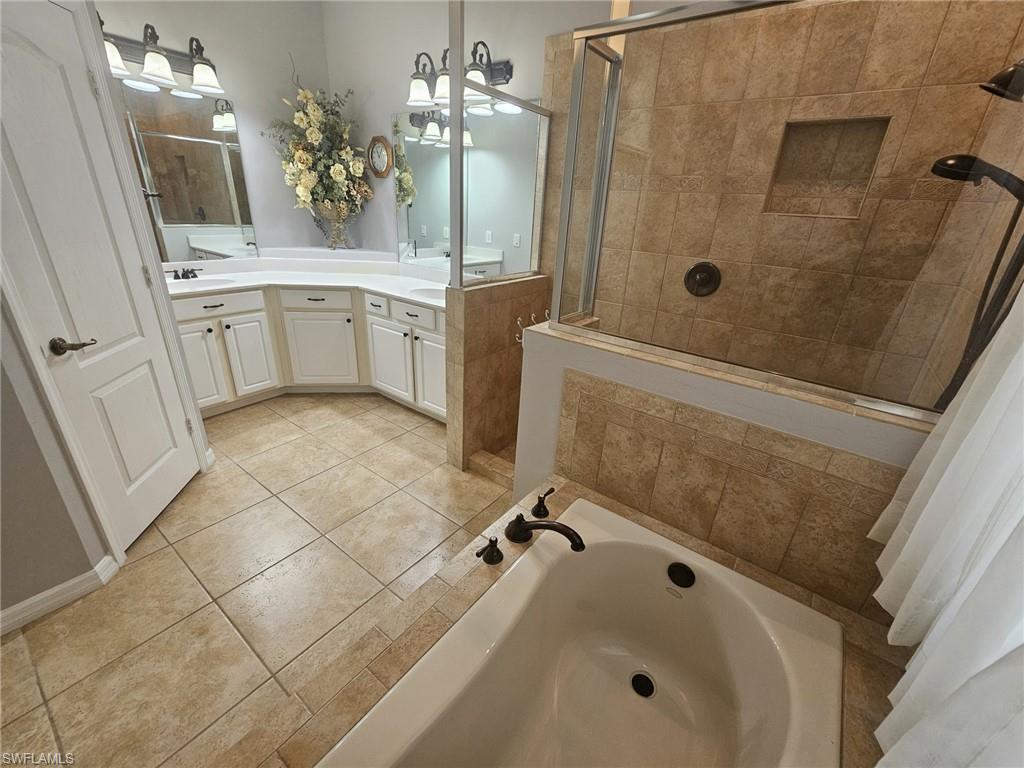 Bathroom featuring a built-in bathtub, a walk-in shower with glass enclosure, dual vanity sinks, and tile flooring