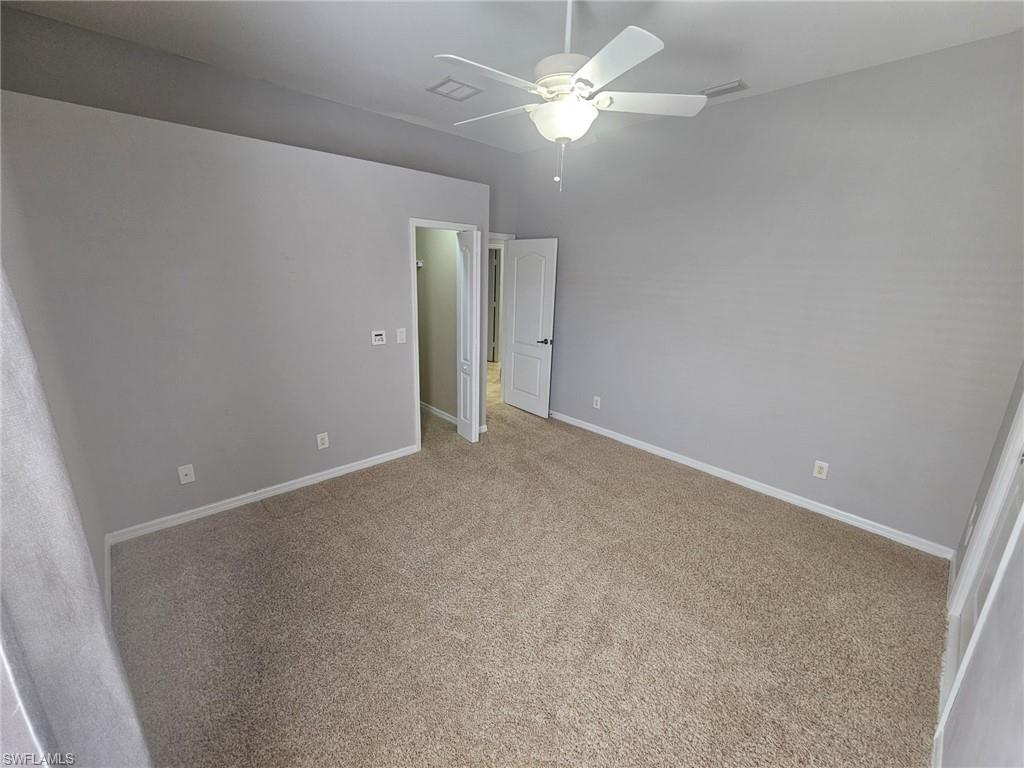 Neutral gray wall paint with white trim, tan carpet flooring, and a ceiling fan with integrated lighting